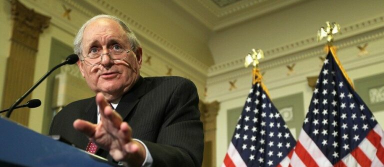 Senator Levin giving a speech flanked by U.S. flags