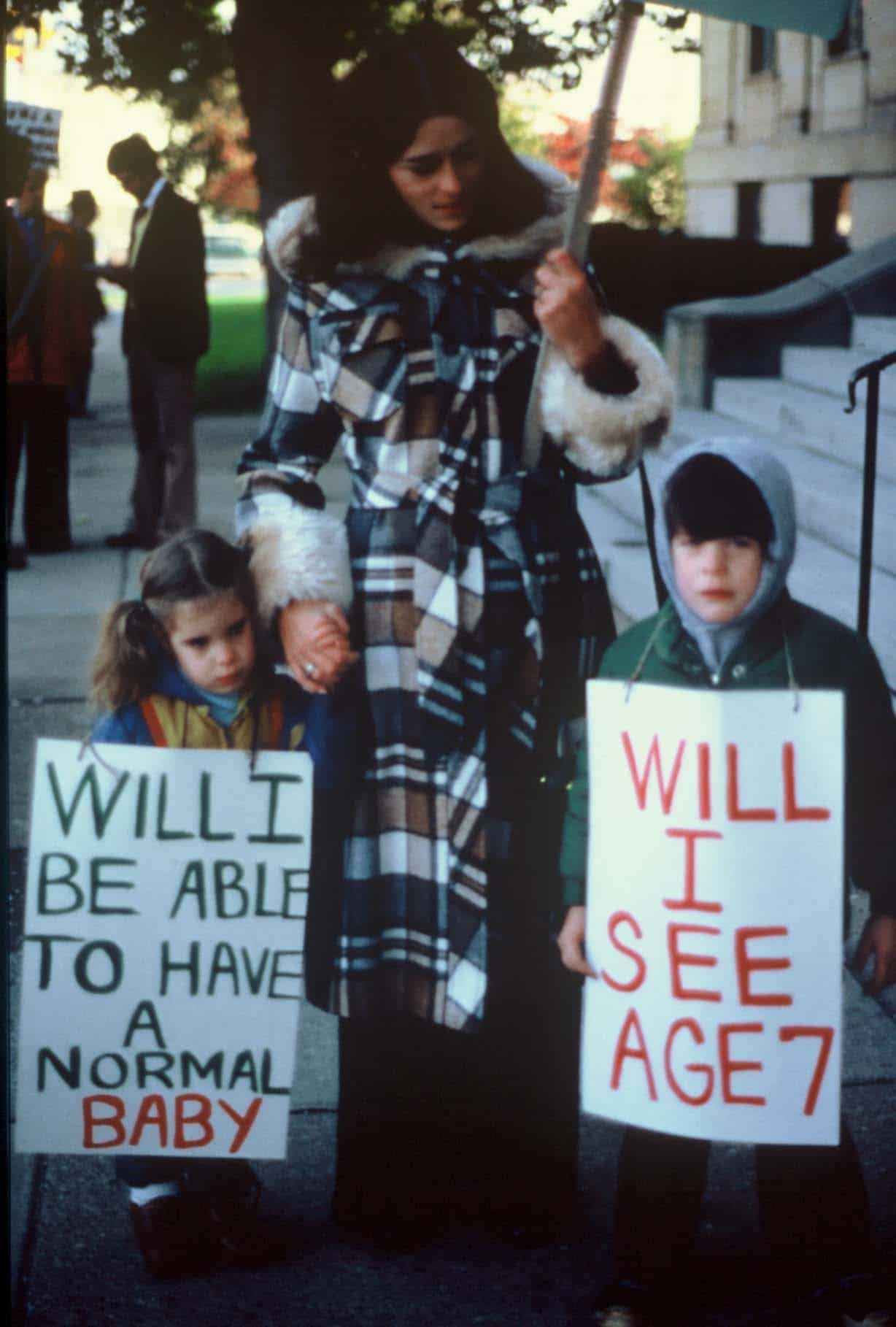 Lois Gibbs and children Image of mother and children. The children are holding signs that say "Will I be able to have a normal baby" and "Will I see age 7"